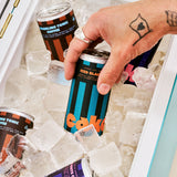 Hand holding a can of iced black coffee over ice cubes with other cans in the background.